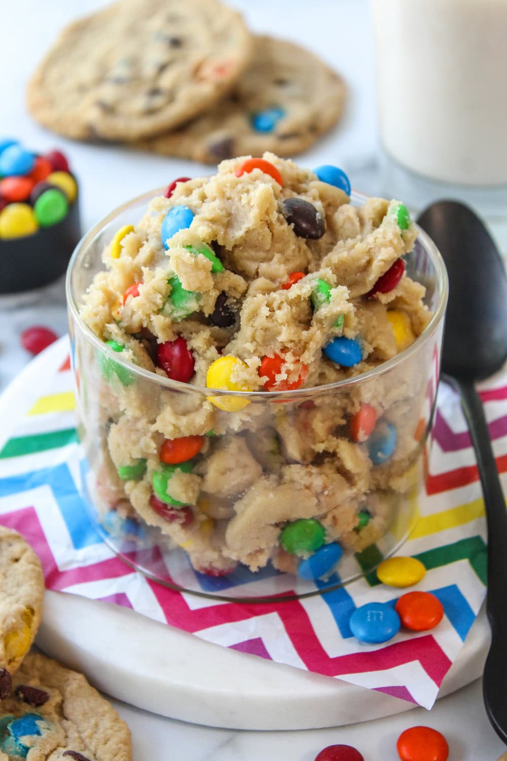 Edible M&M cookie dough served in bowl with spoon on table