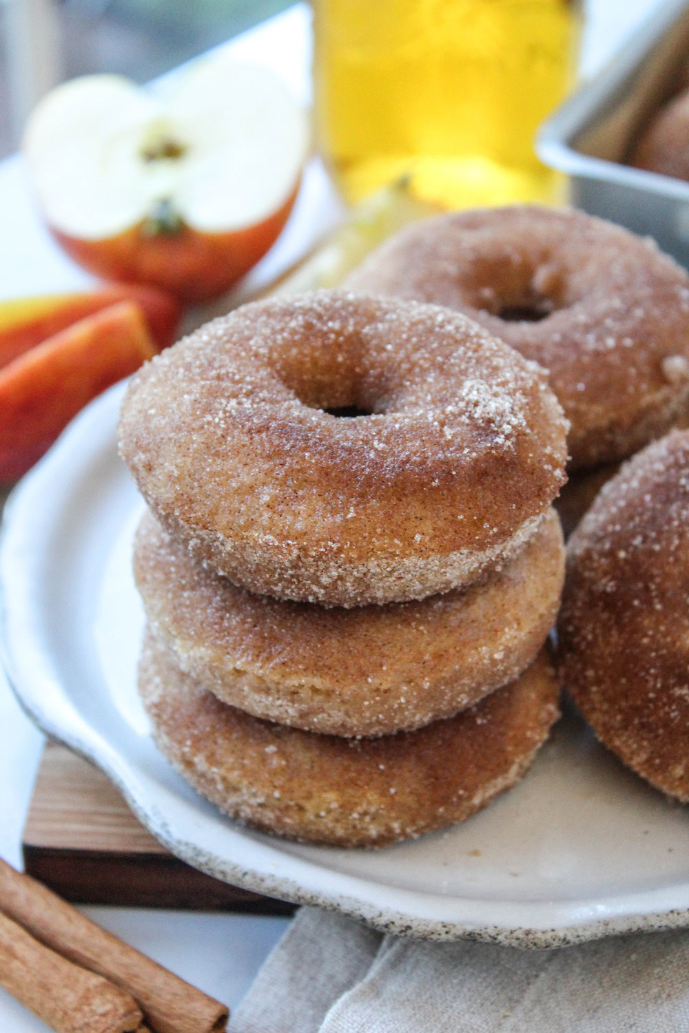 Baked apple cider donuts coated in cinnamon sugar, stacked on a plate with a golden-brown finish