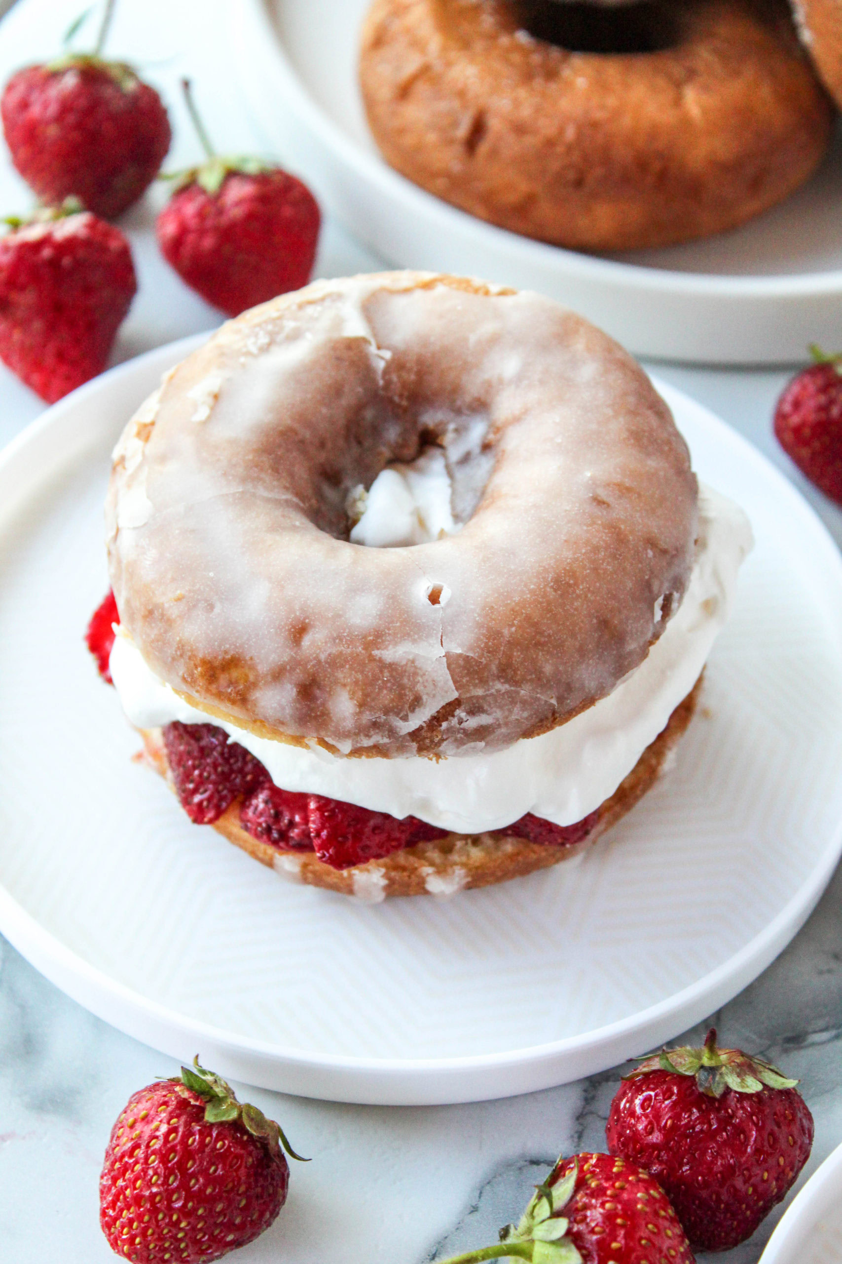 layering strawberries and whipped cream on donut halves