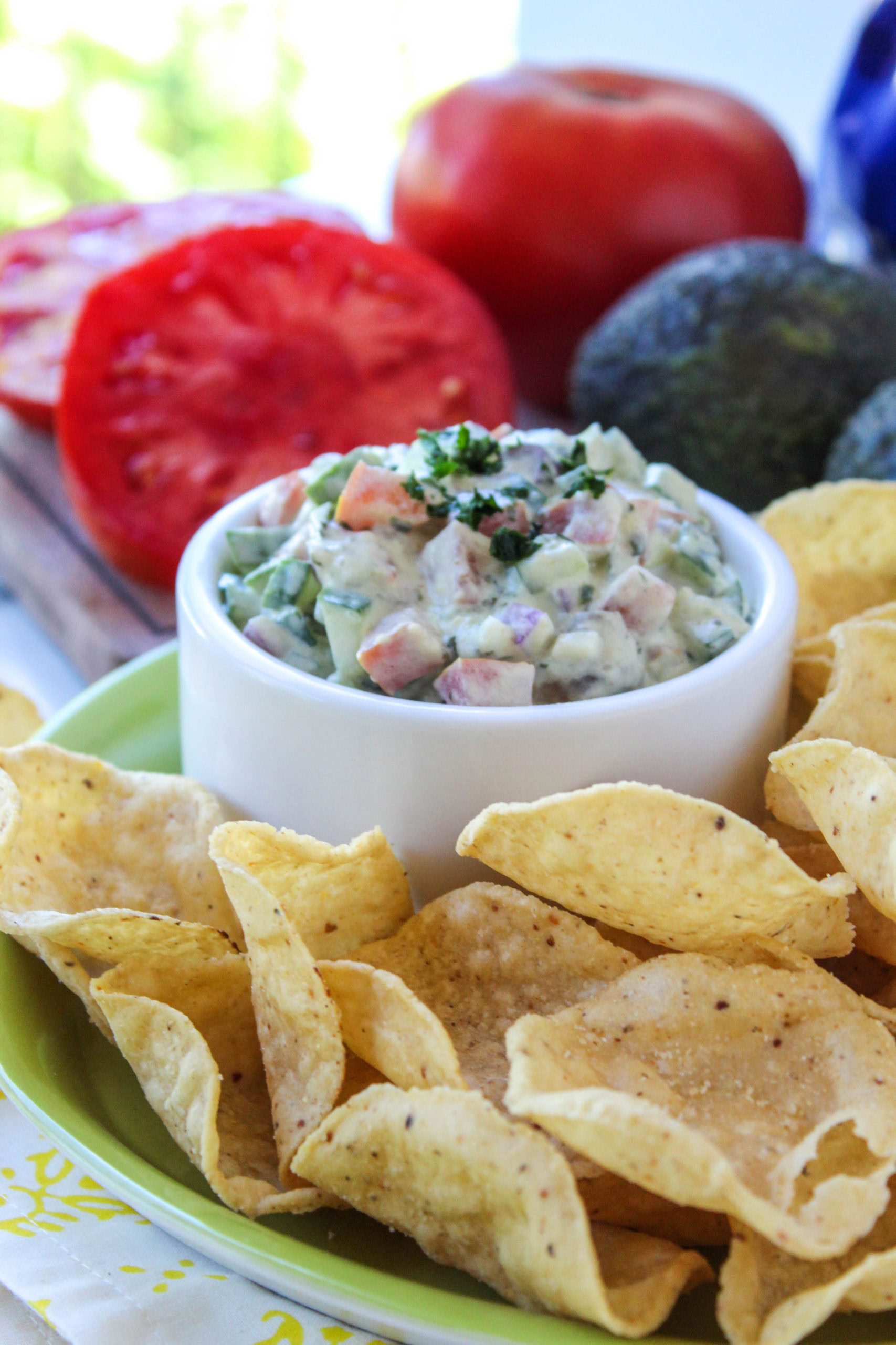 Cucumber avocado salsa in a bowl with fresh tomatoes, red onion, and cilantro