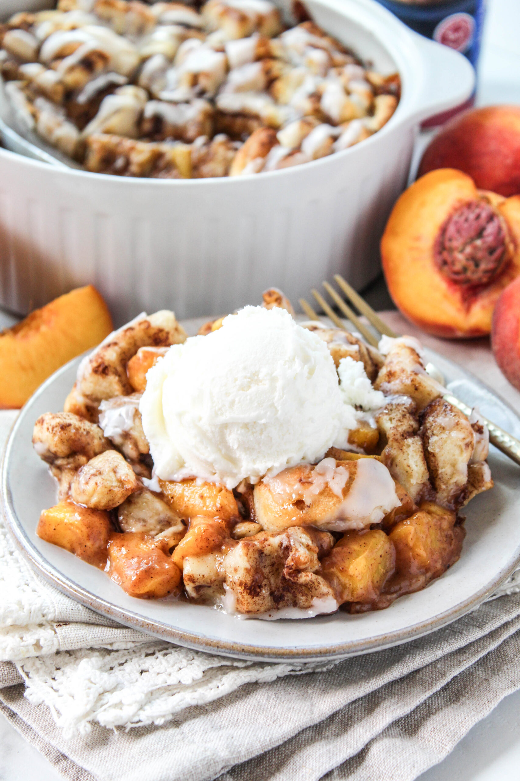 Warm cinnamon roll peach cobbler topped with creamy icing and served on a plate