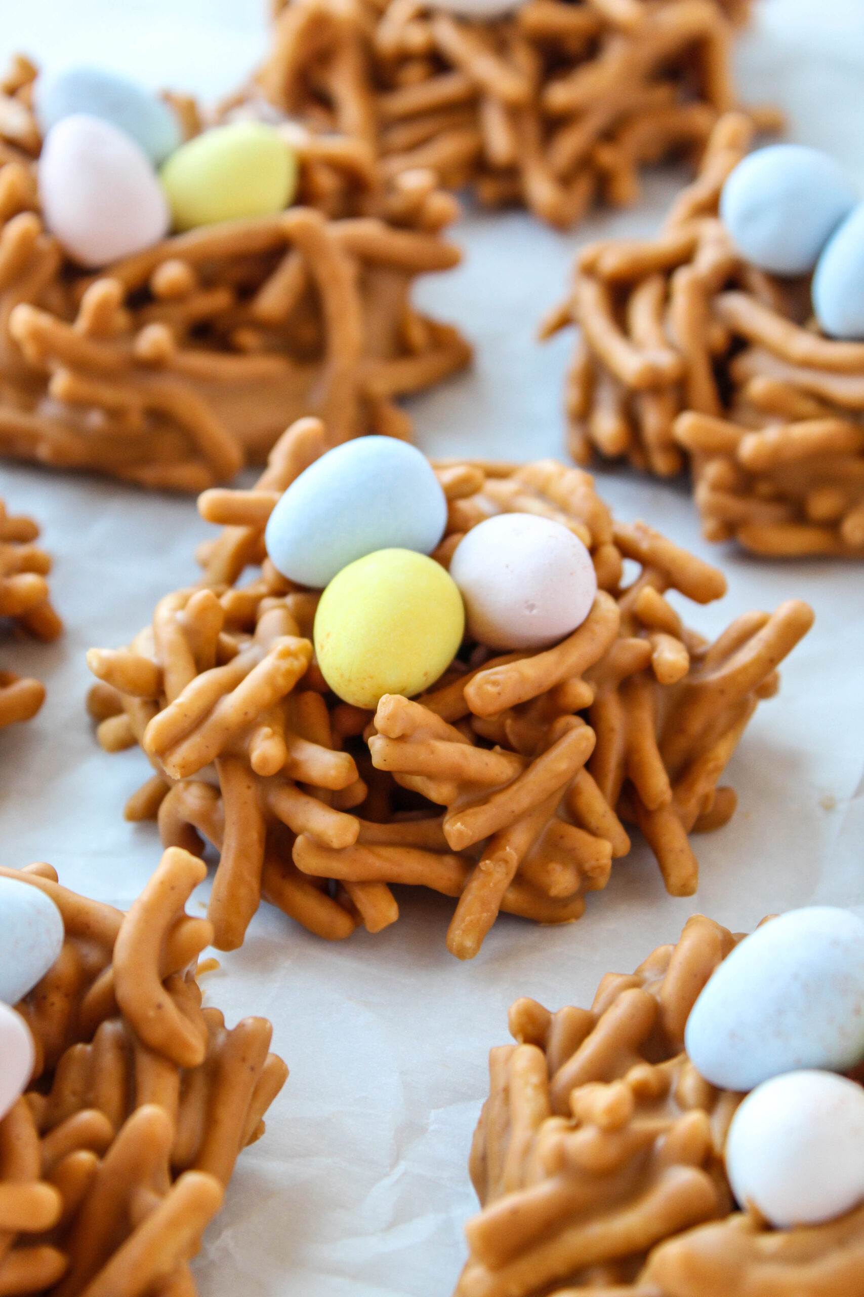 Butterscotch and peanut butter bird nest cookies topped with chocolate eggs on parchment paper.