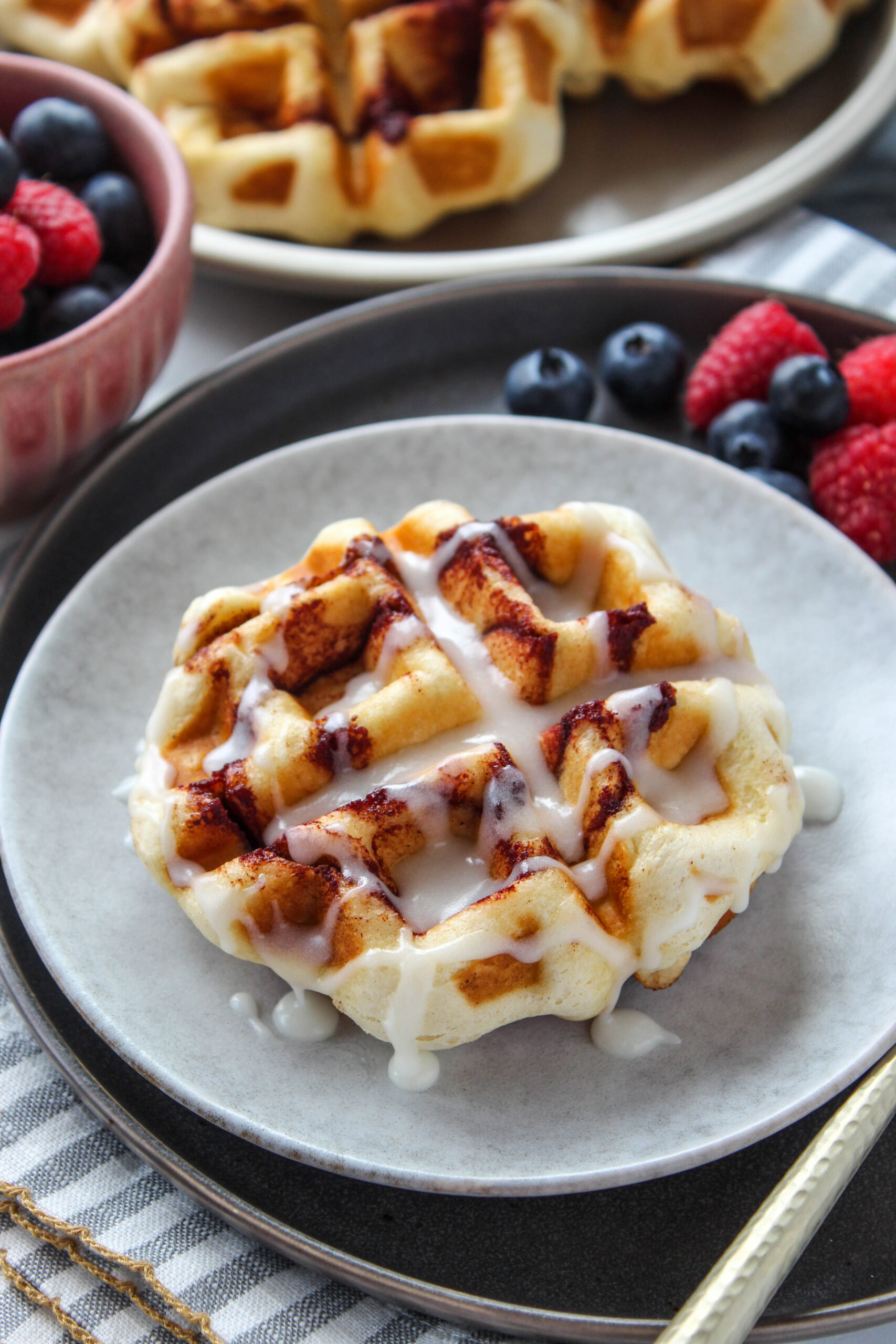Golden cinnamon roll waffles made in a waffle maker and topped with glaze