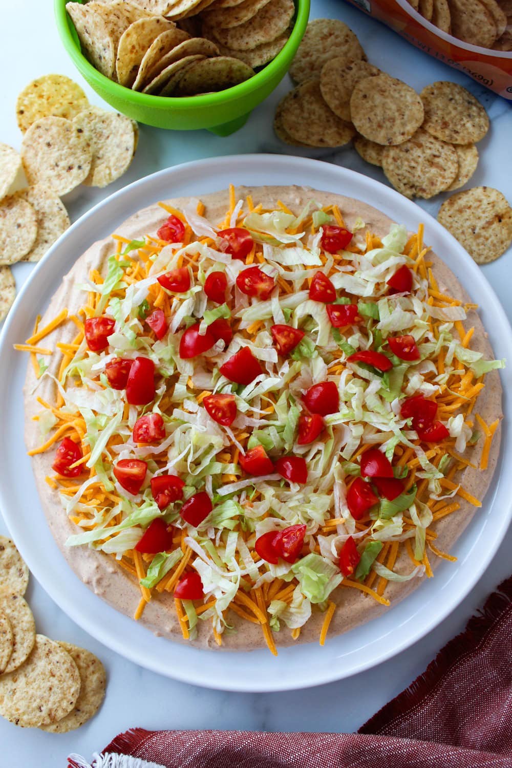Homemade taco dip topped with shredded cheddar cheese, diced tomatoes, and fresh lettuce