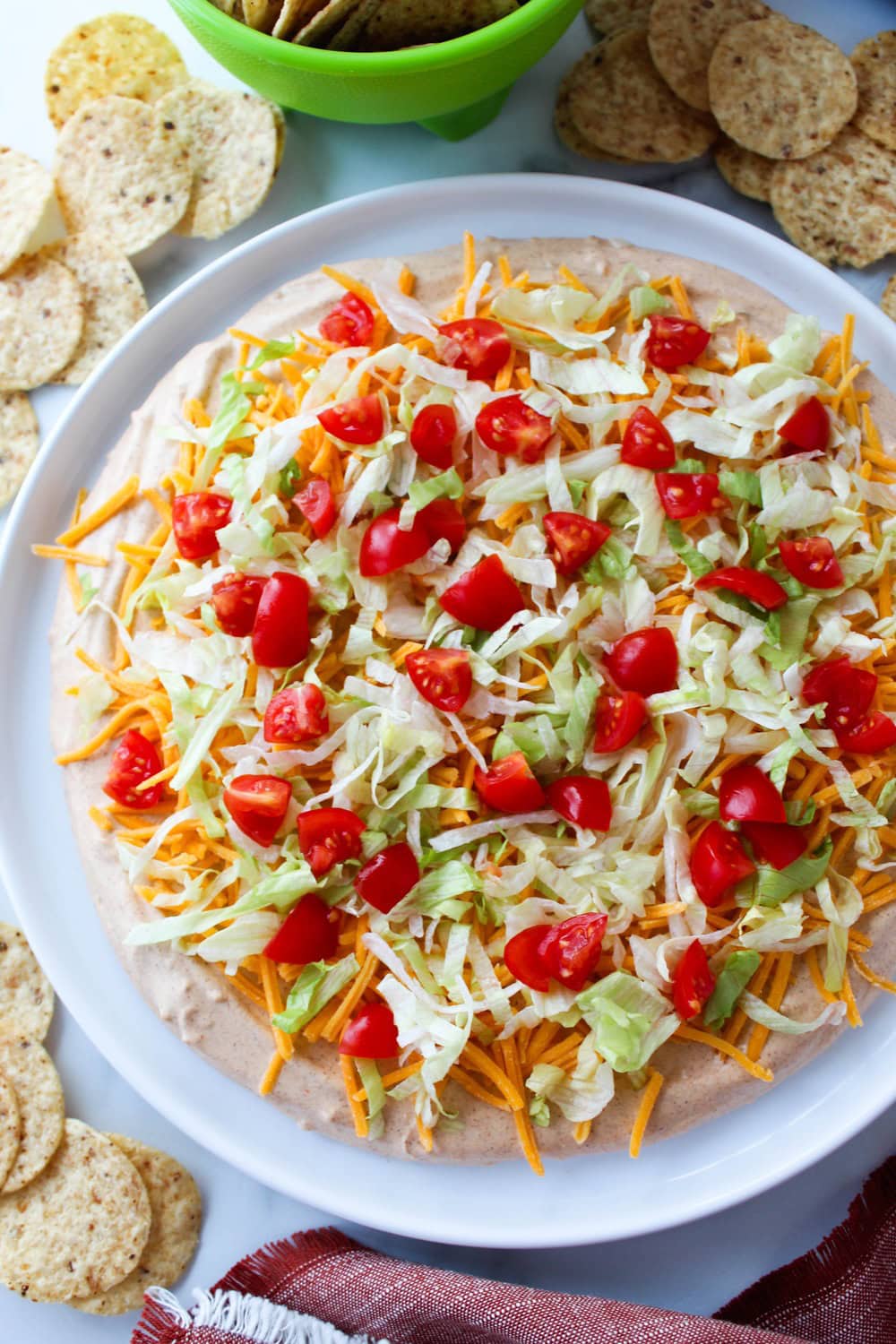 Creamy taco dip with taco seasoning, cheese, lettuce, and tomatoes ready for dipping