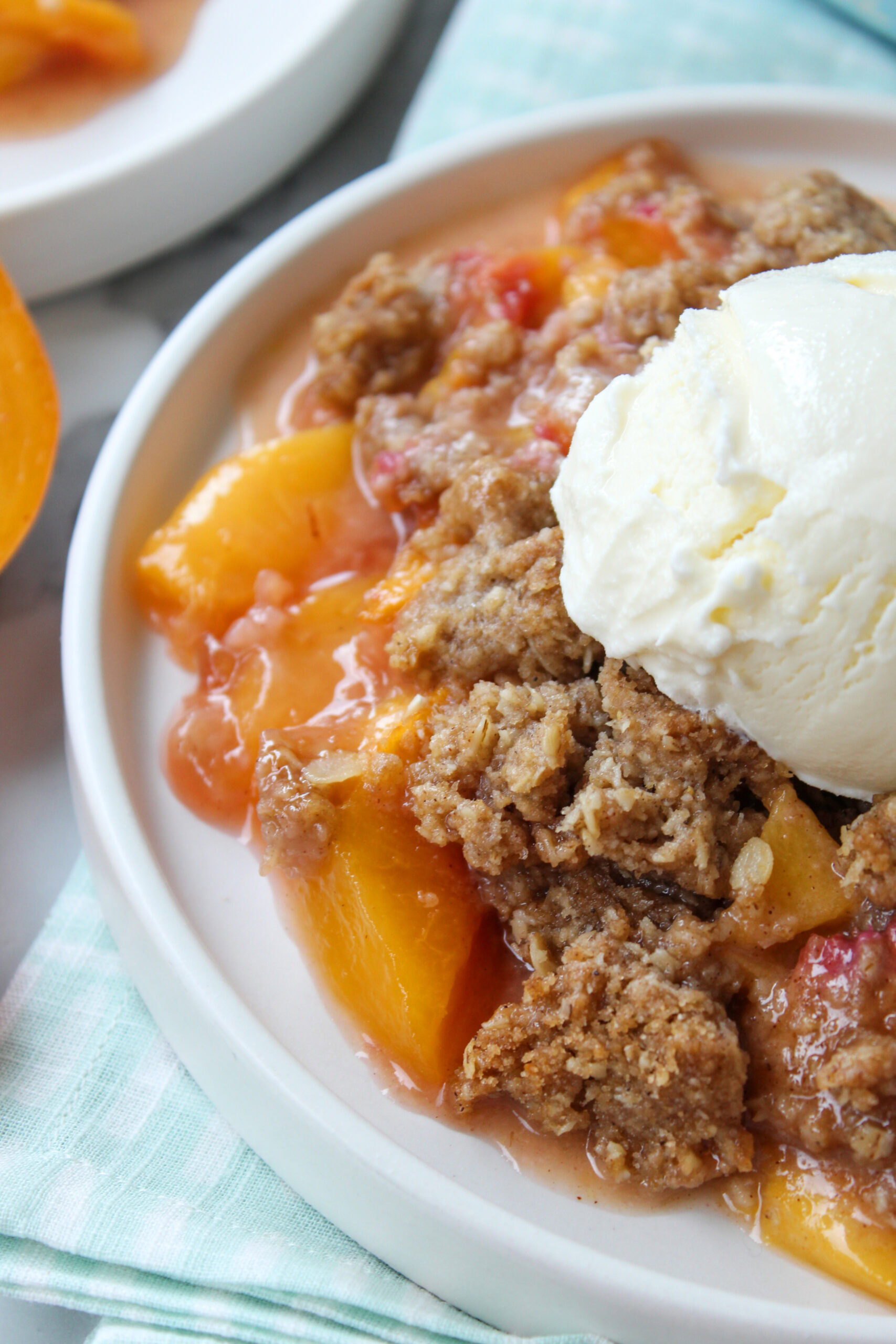 Serving of peach crisp scooped into a bowl, showing tender peaches beneath a crisp oat topping