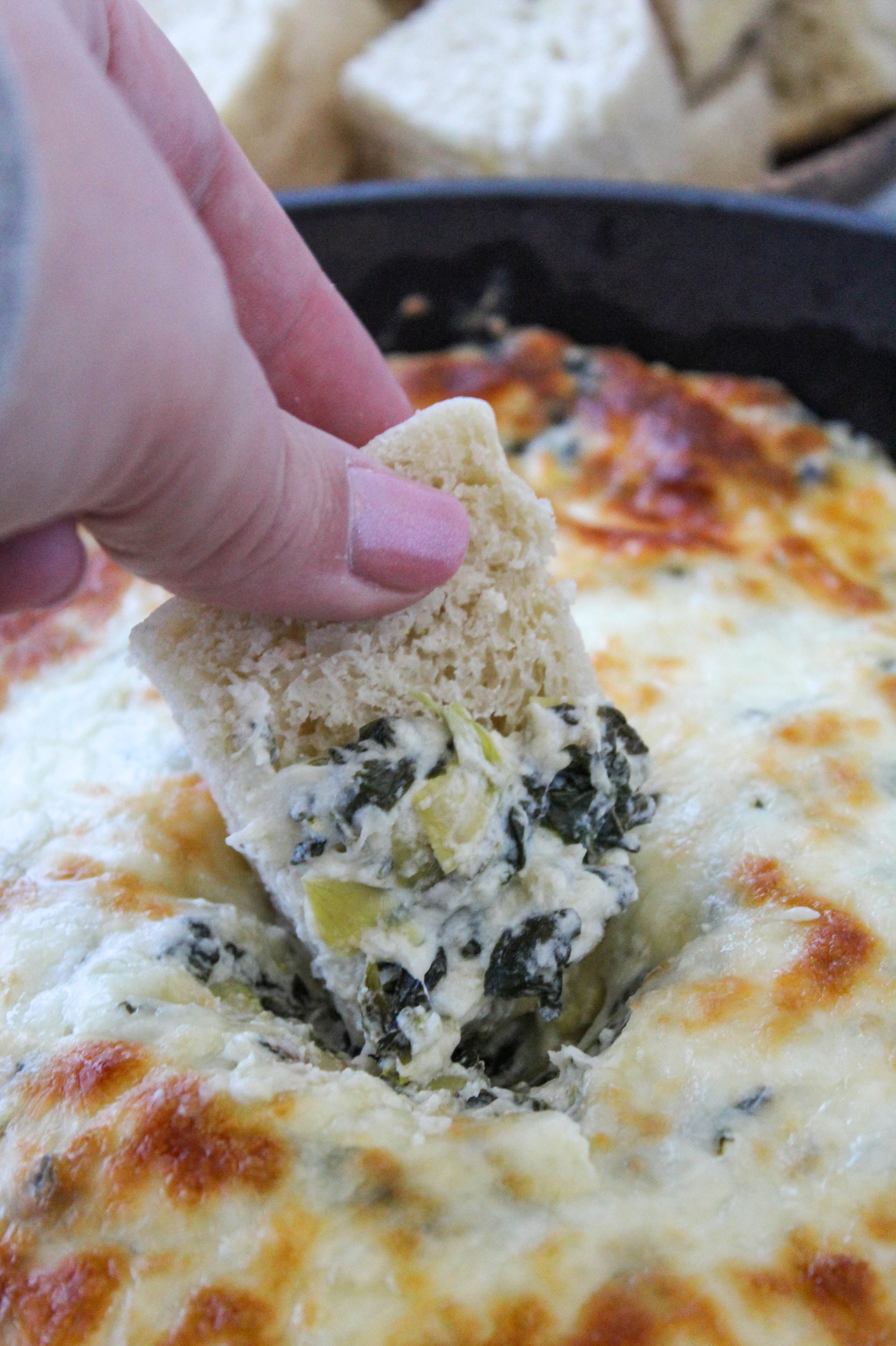 Scooping creamy spinach artichoke dip from a baking dish