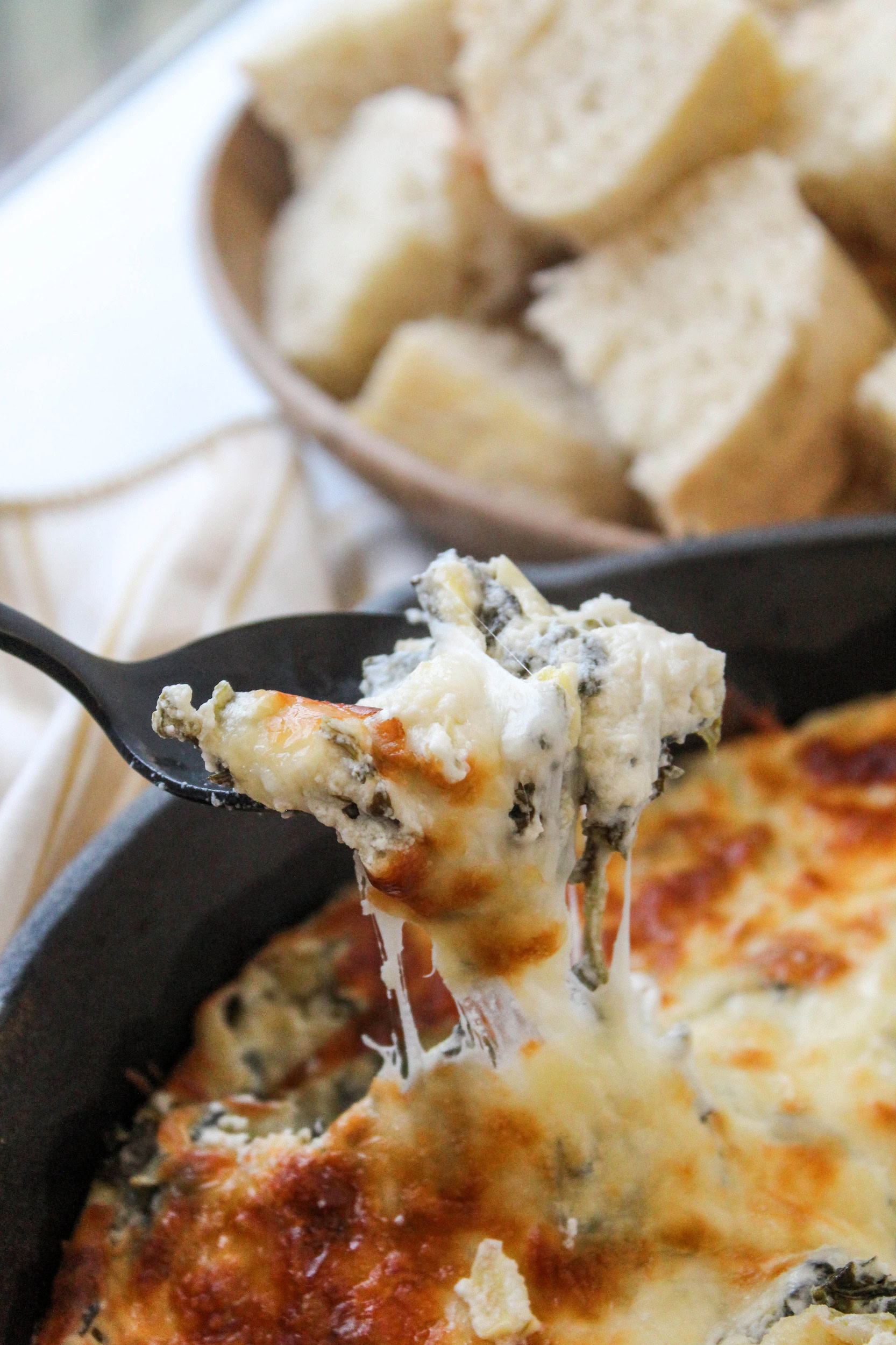 Creamy spinach artichoke dip in a rustic pan with a spoon