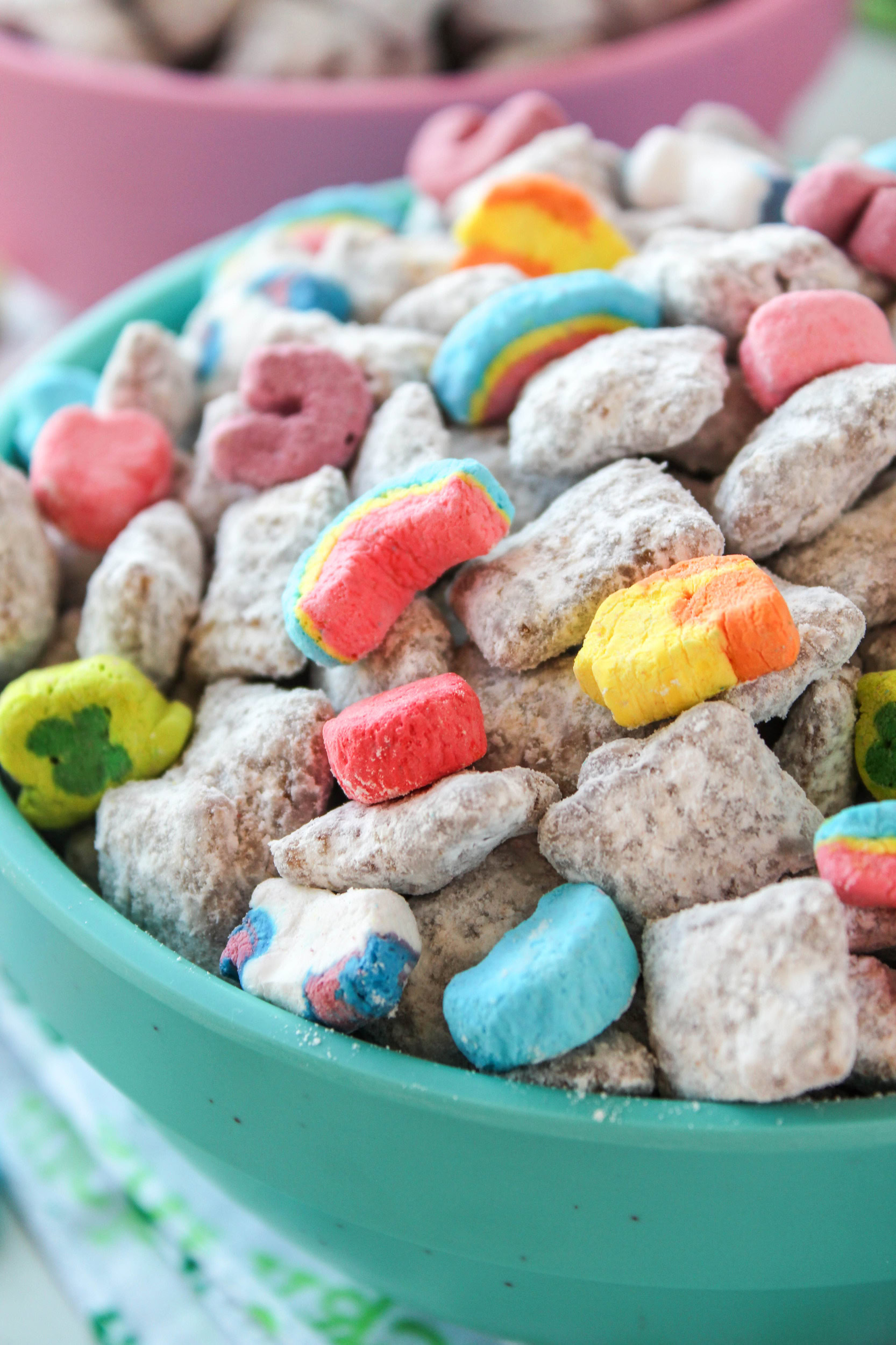 Lucky Charms puppy chow with chocolate-coated cereal dusted in powdered sugar and topped with colorful marshmallows