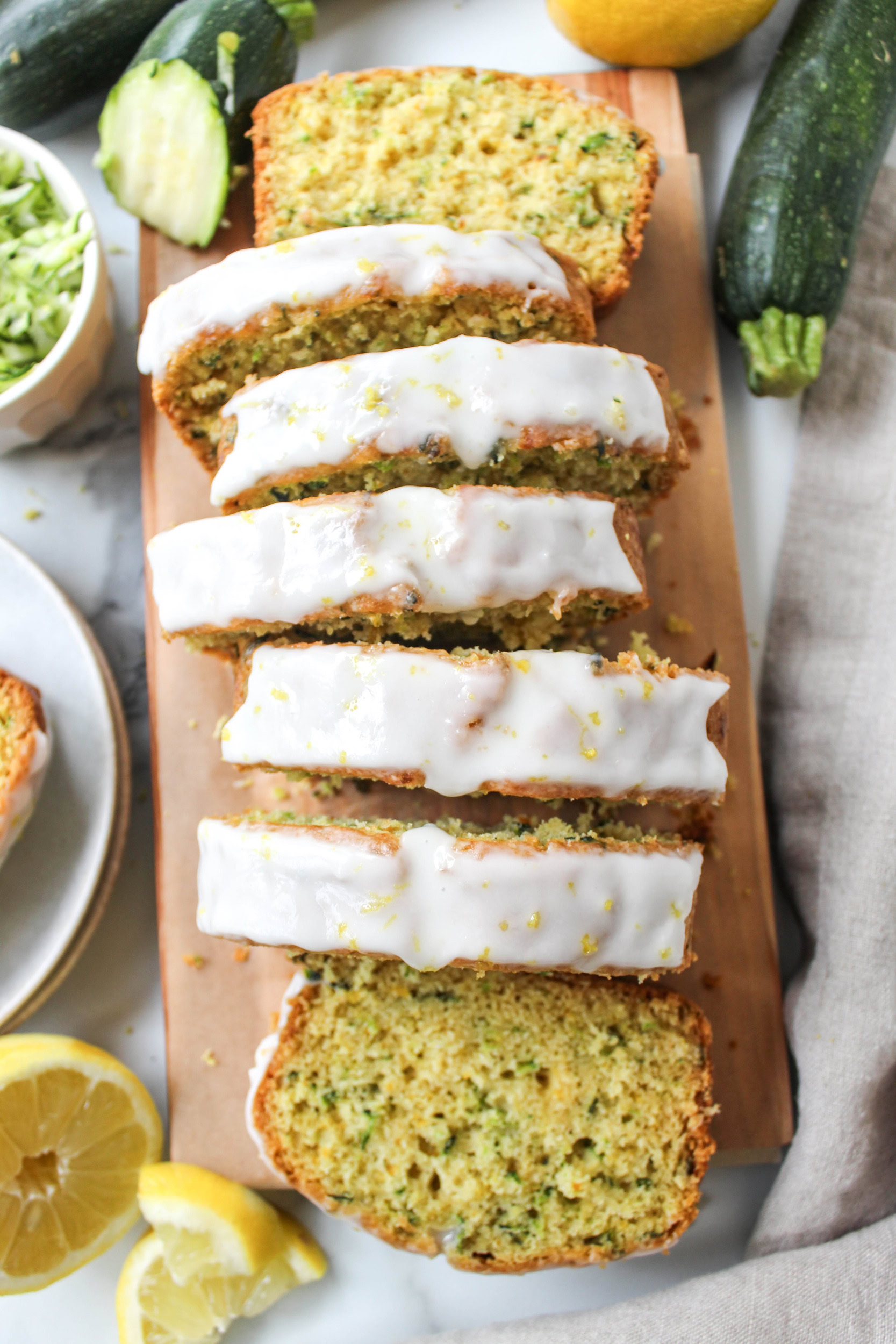 Glazed lemon zucchini bread topped with fresh lemon zest and sliced on a wooden cutting board