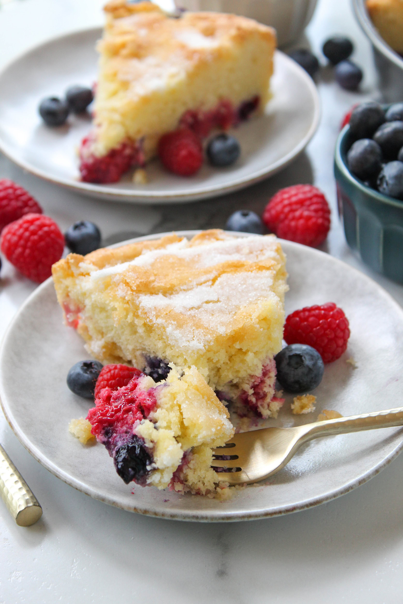 fork cutting into soft mixed berry cake with juicy berries