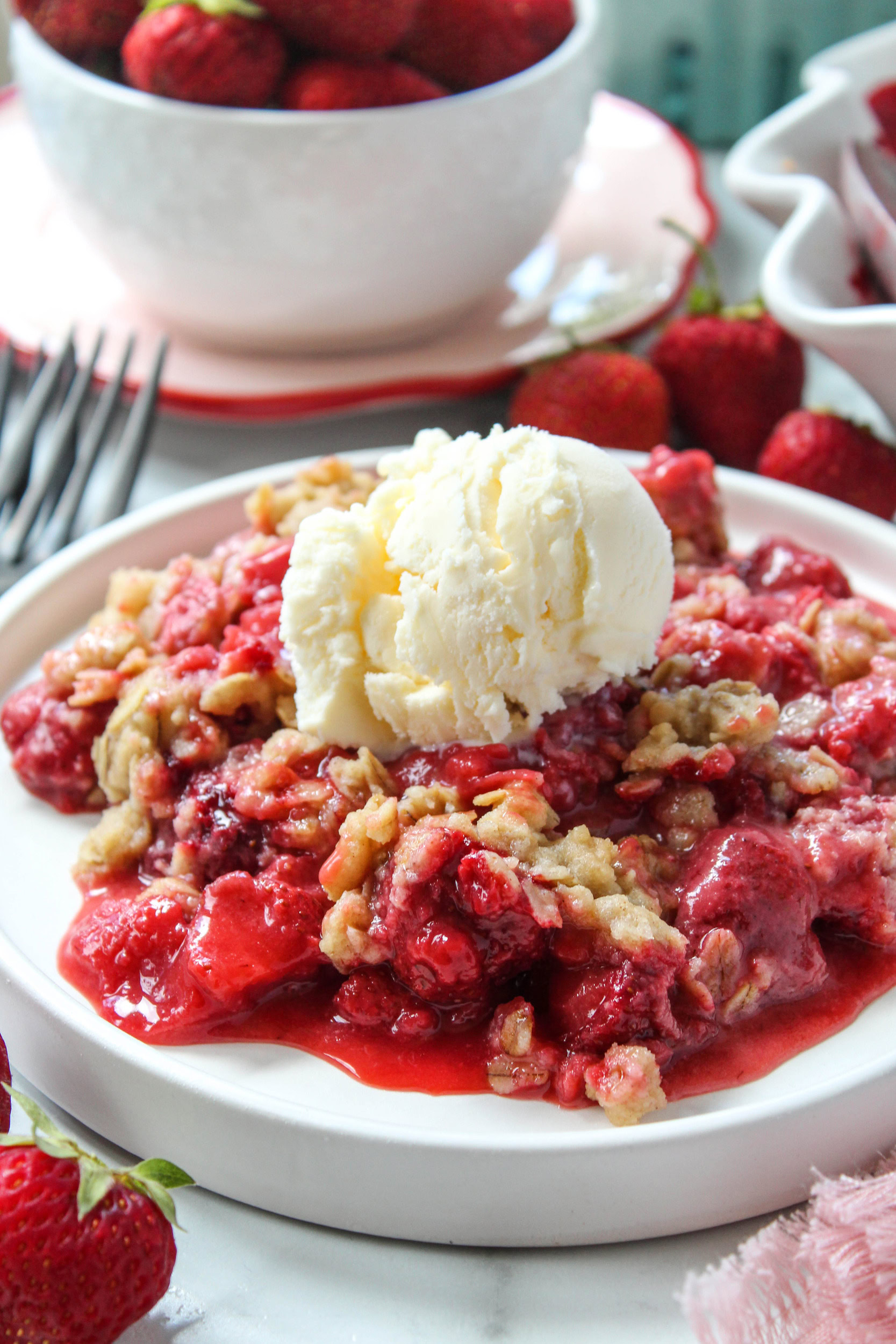 Warm strawberry crisp topped with vanilla ice cream melting over a buttery oat crumble
