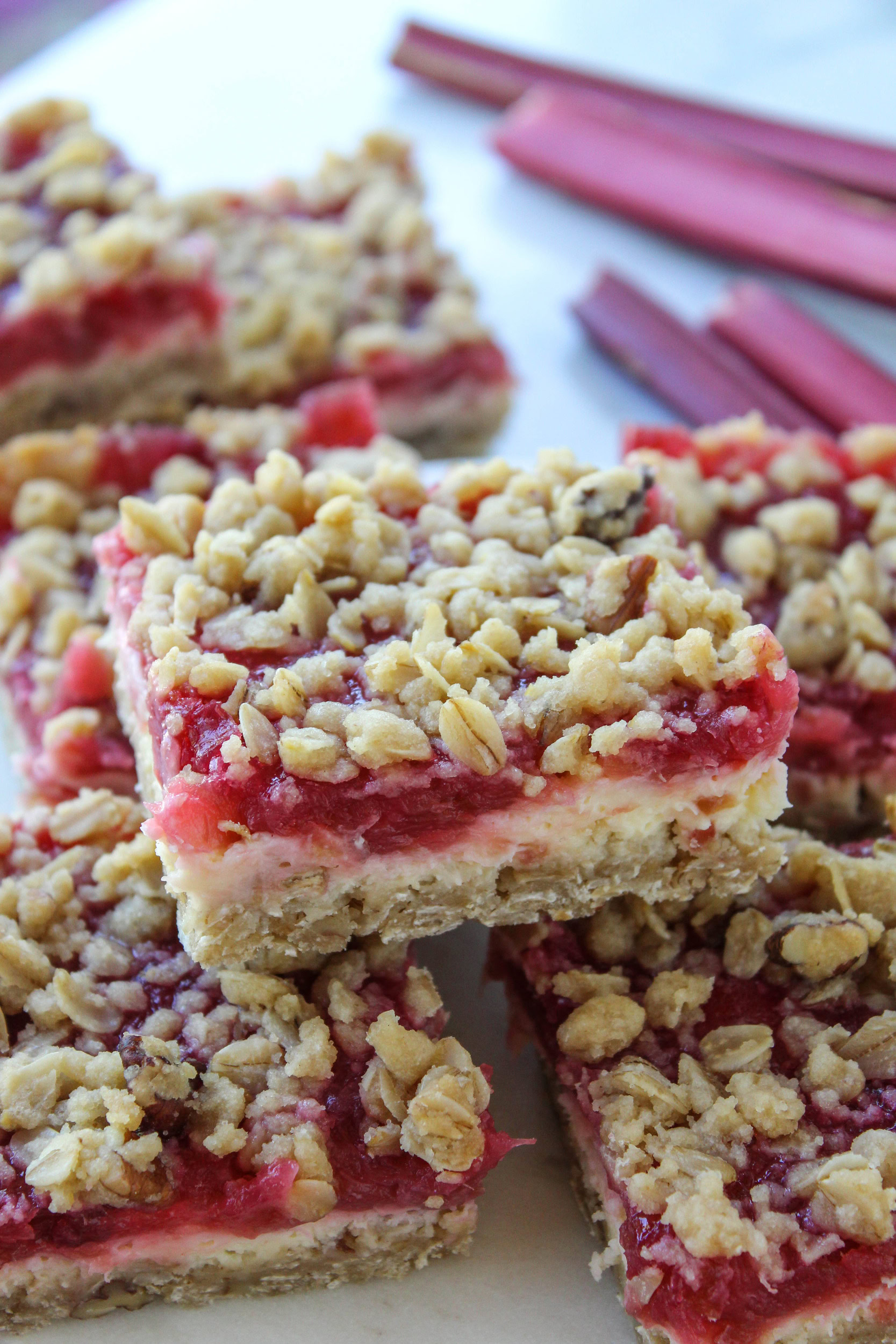 Close-up of rhubarb cheesecake bars with creamy cheesecake layer, bright pink rhubarb topping, and golden crumble crust
