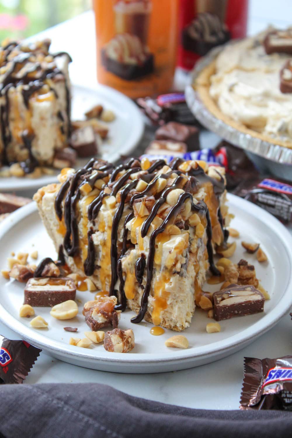 Slice of no-bake Snickers pie topped with chocolate drizzle, caramel, and chopped peanuts